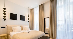 A modern hotel room with a large bed, a bedside table, a wall-mounted light fixture, and a window with curtains. - UrbanFlat 197 - Appartement Saint Honoré Champs Elysées (París)