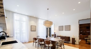 Un comedor moderno con una mesa y sillas de madera, una lámpara colgante y vista al espacio de estar contiguo.