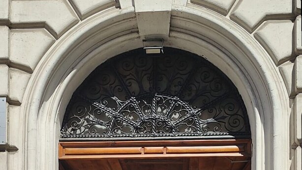 Un arco de entrada con un adorno metálico decorativo, puertas de madera y piso de baldosas.