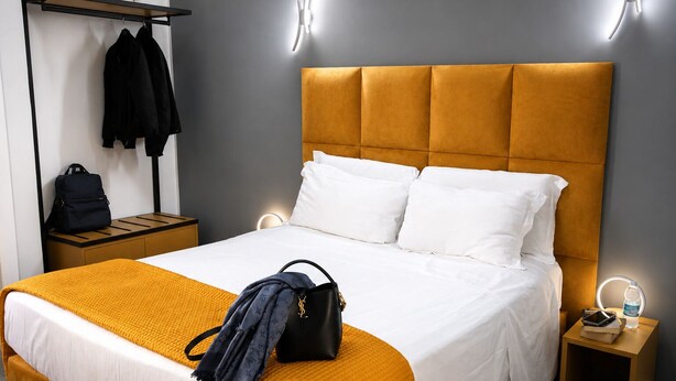 Ein Hotelzimmer mit einem Bett, einem Nachttisch, einem Kleiderhaken und einer Wandleuchte.
