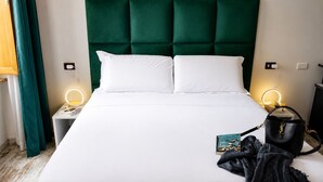 Una cama con cabecera tapizada de verde, ropa de cama blanca y dos lámparas de noche.
