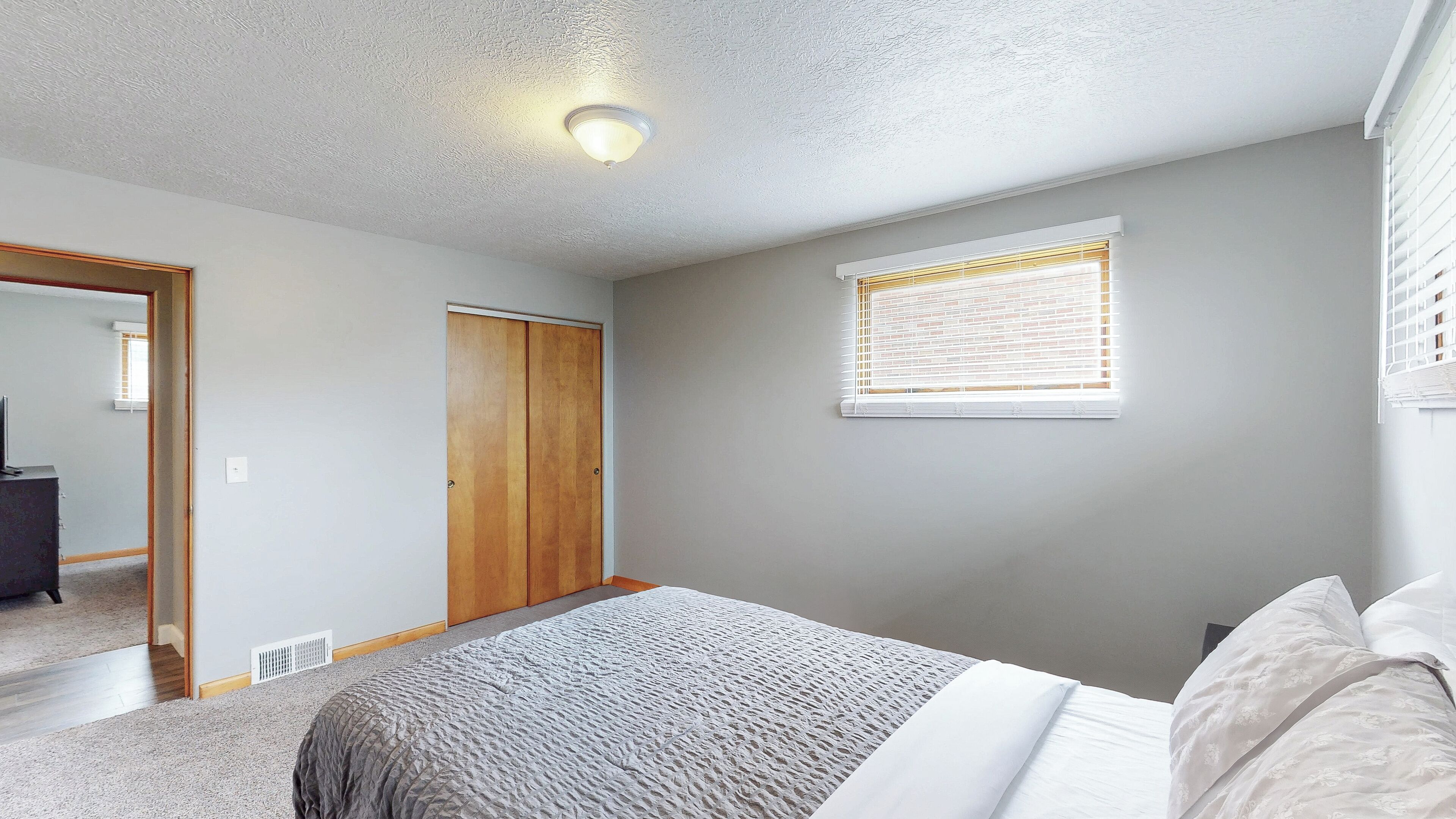 A bedroom with a bed, a wardrobe, a window with blinds, and a ceiling light.