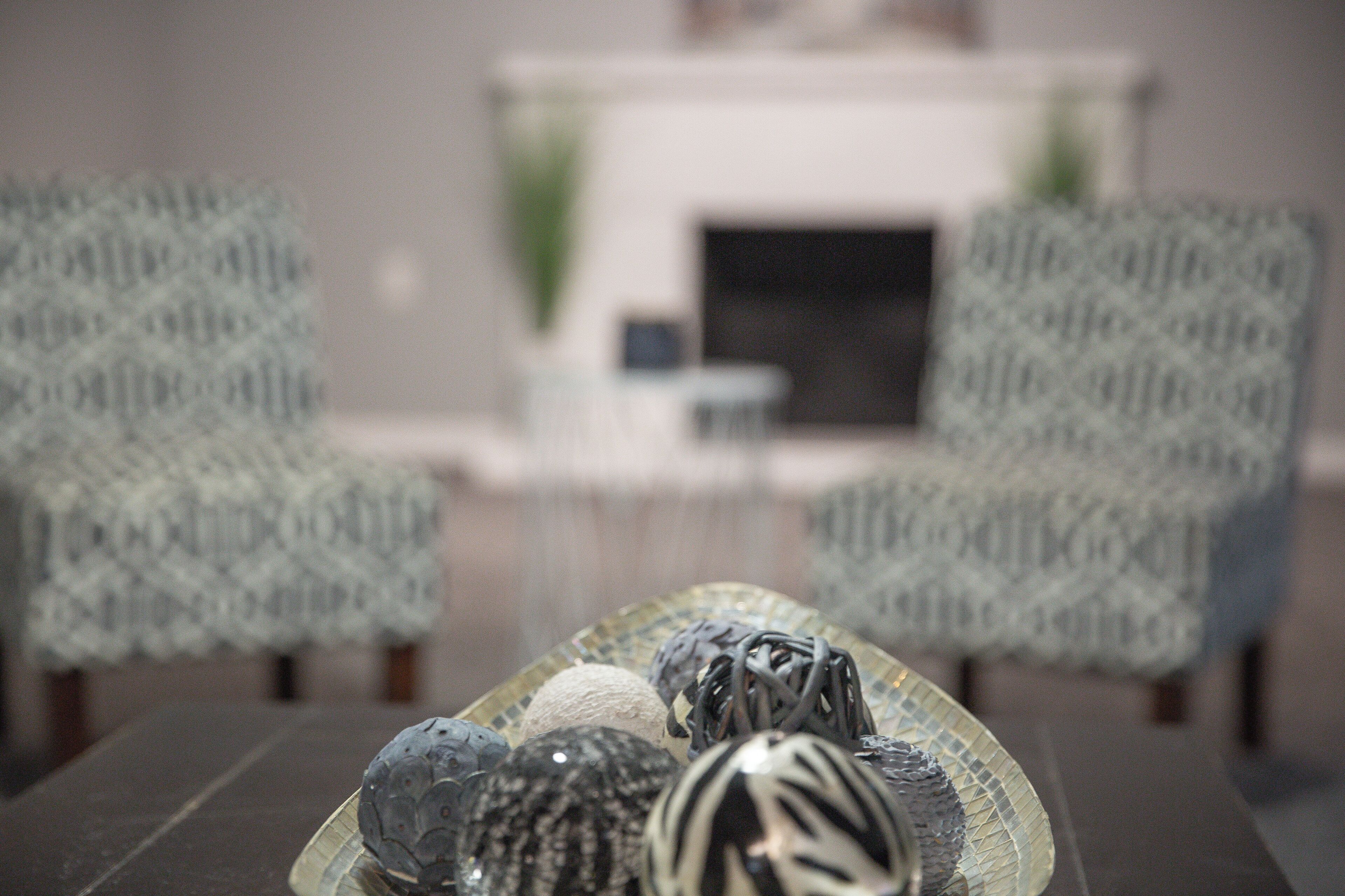 Une pièce avec des chaises à motifs, une table en verre ornée d’objets décoratifs et une cheminée en arrière-plan.