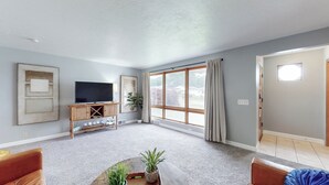 Ein Wohnzimmer mit Fernseher, einem Couchtisch mit Pflanzen und einem großen Fenster mit Vorhängen.