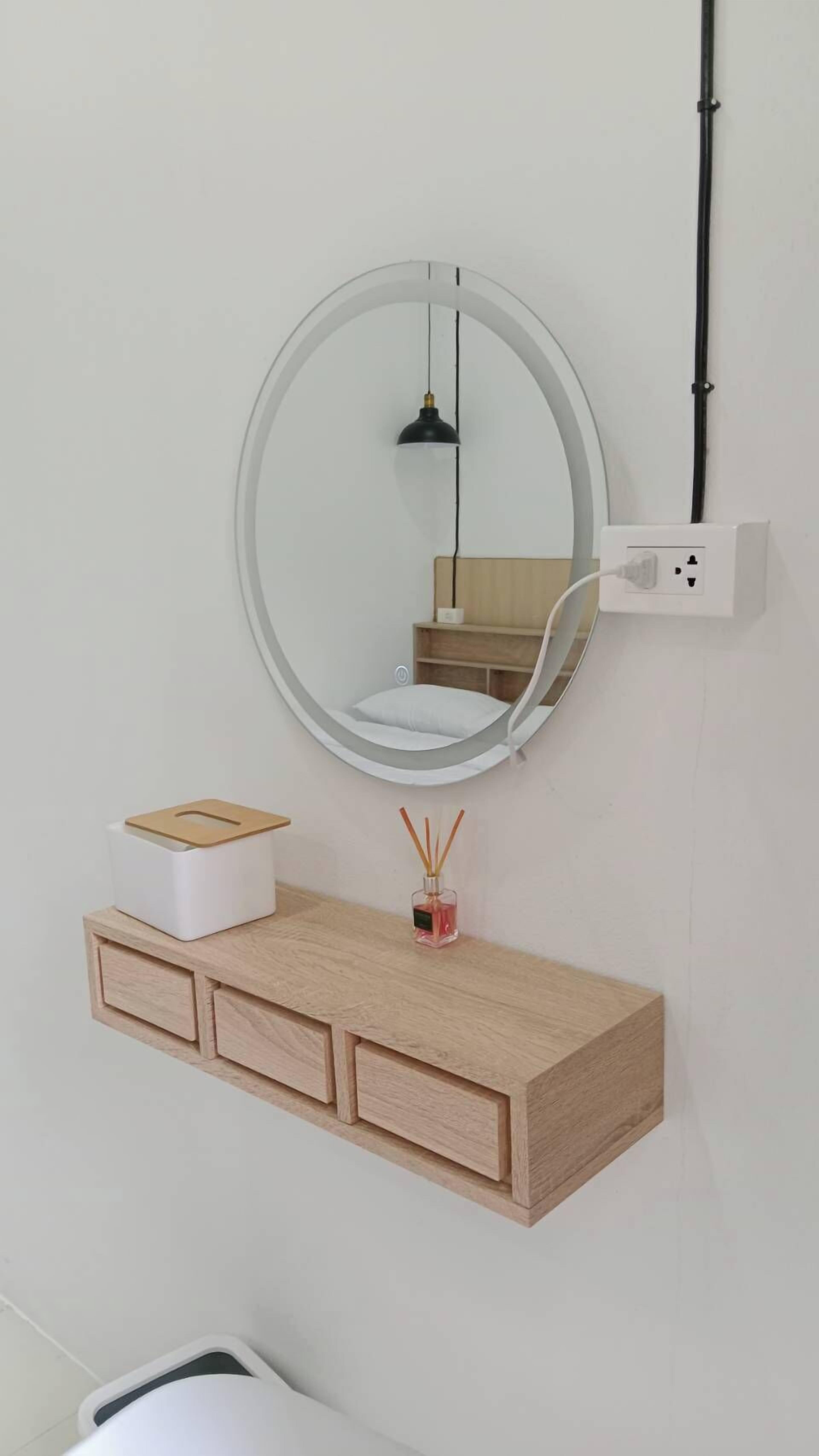 Un baño con un espejo redondo, un tocador de madera, una lámpara colgante y un enchufe.
