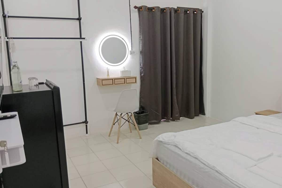 Un dormitorio con cama, mesita de noche, espejo, cómoda y cortina.