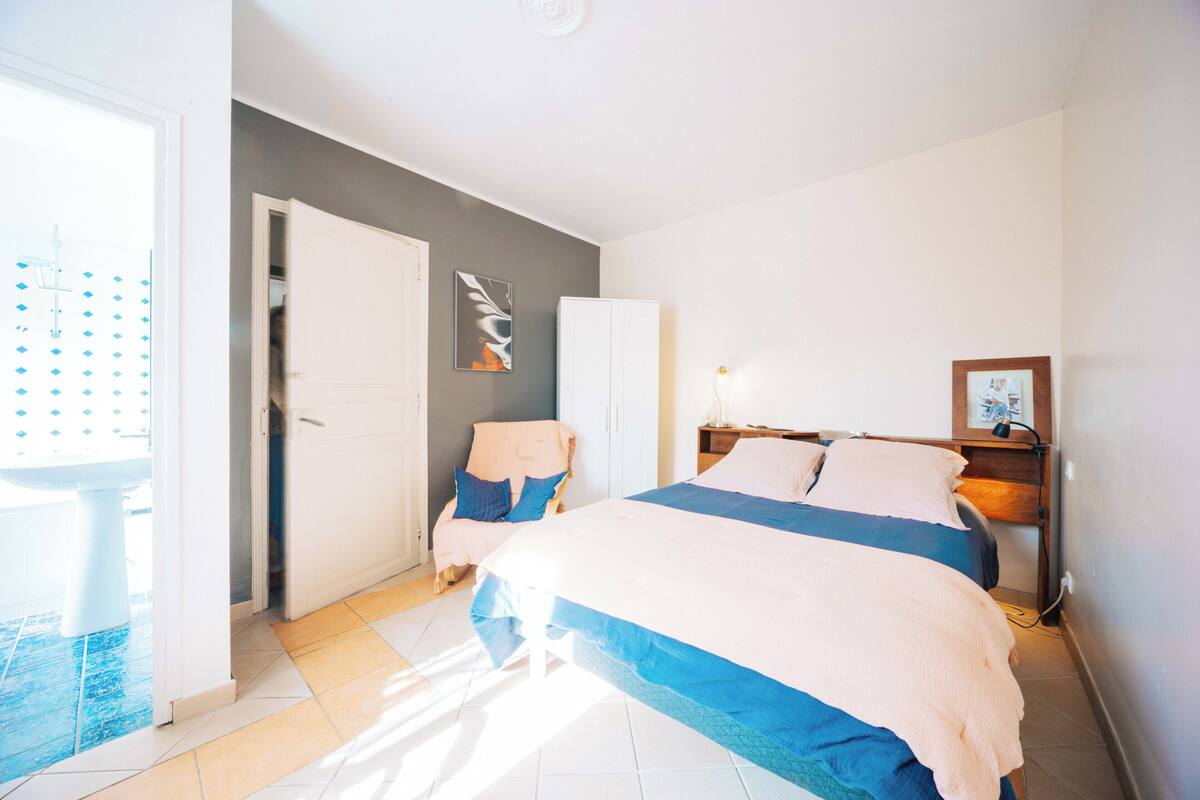 A bedroom with a bed, a chair, a wardrobe, and a door leading to a bathroom.