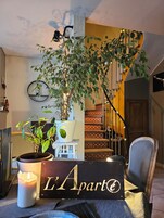 Una sala de estar acogedora con una escalera, una planta en maceta, una vela y un cartel que dice "L'Aparté".