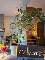 Interior de restaurante con una pizarra de menú, una planta en maceta, una copa de vino y un letrero que dice "L'Aparté".
