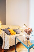 Una habitación con un sofá a rayas, una mesa de centro de vidrio y un jarrón con flores secas.