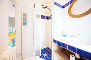 Un baño con cabina de ducha de vidrio, un lavabo blanco y una salpicadura trasera de azulejos azules, además de un estante de madera.