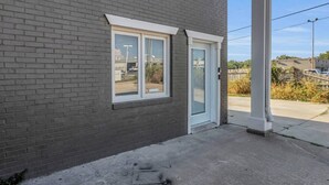 Un bâtiment à l’extérieur en briques sombres, doté d’une fenêtre à cadre blanc et d’une porte en verre.
