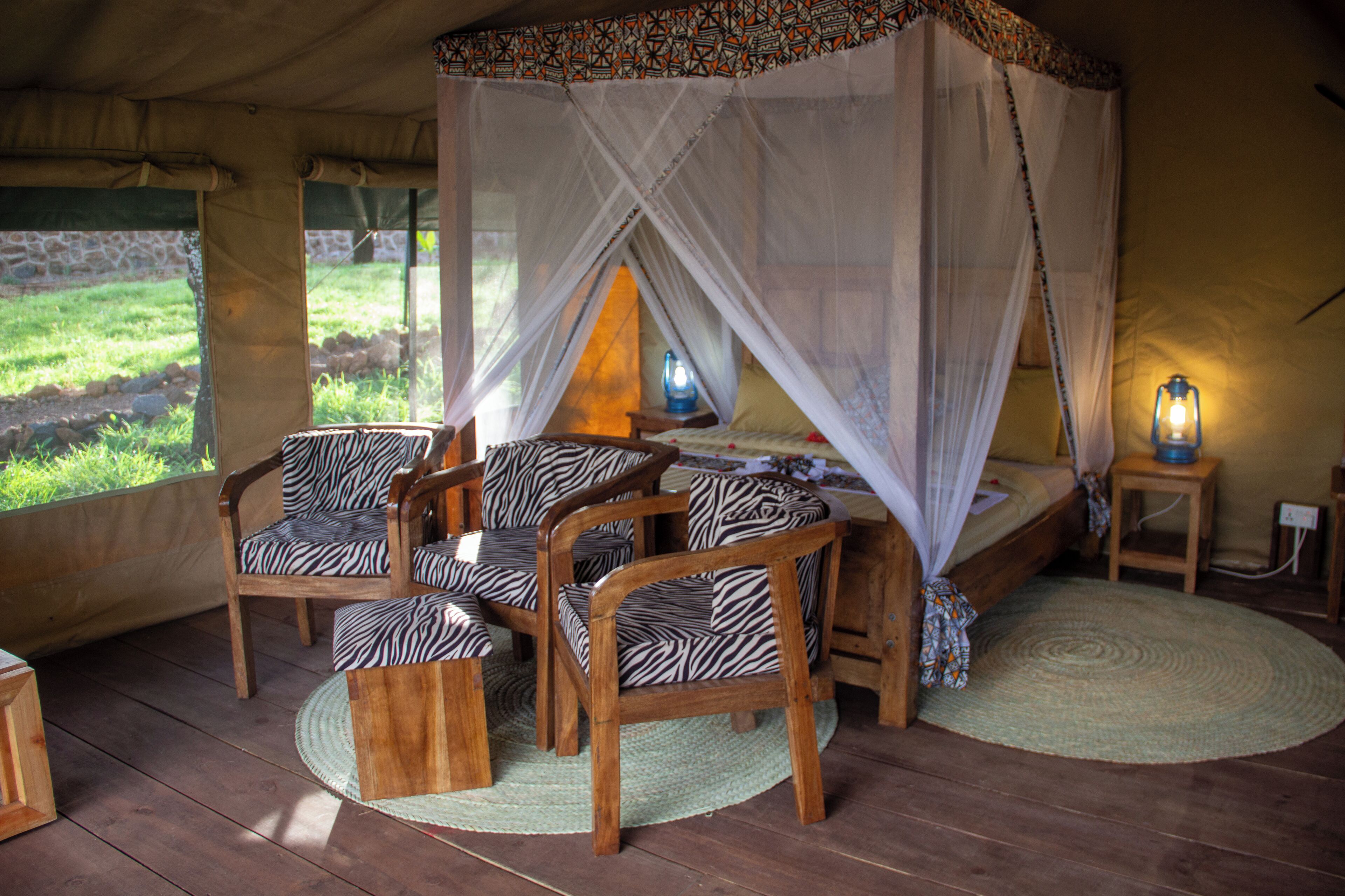 A tent with a bed, zebra-patterned chairs, and a mosquito net.