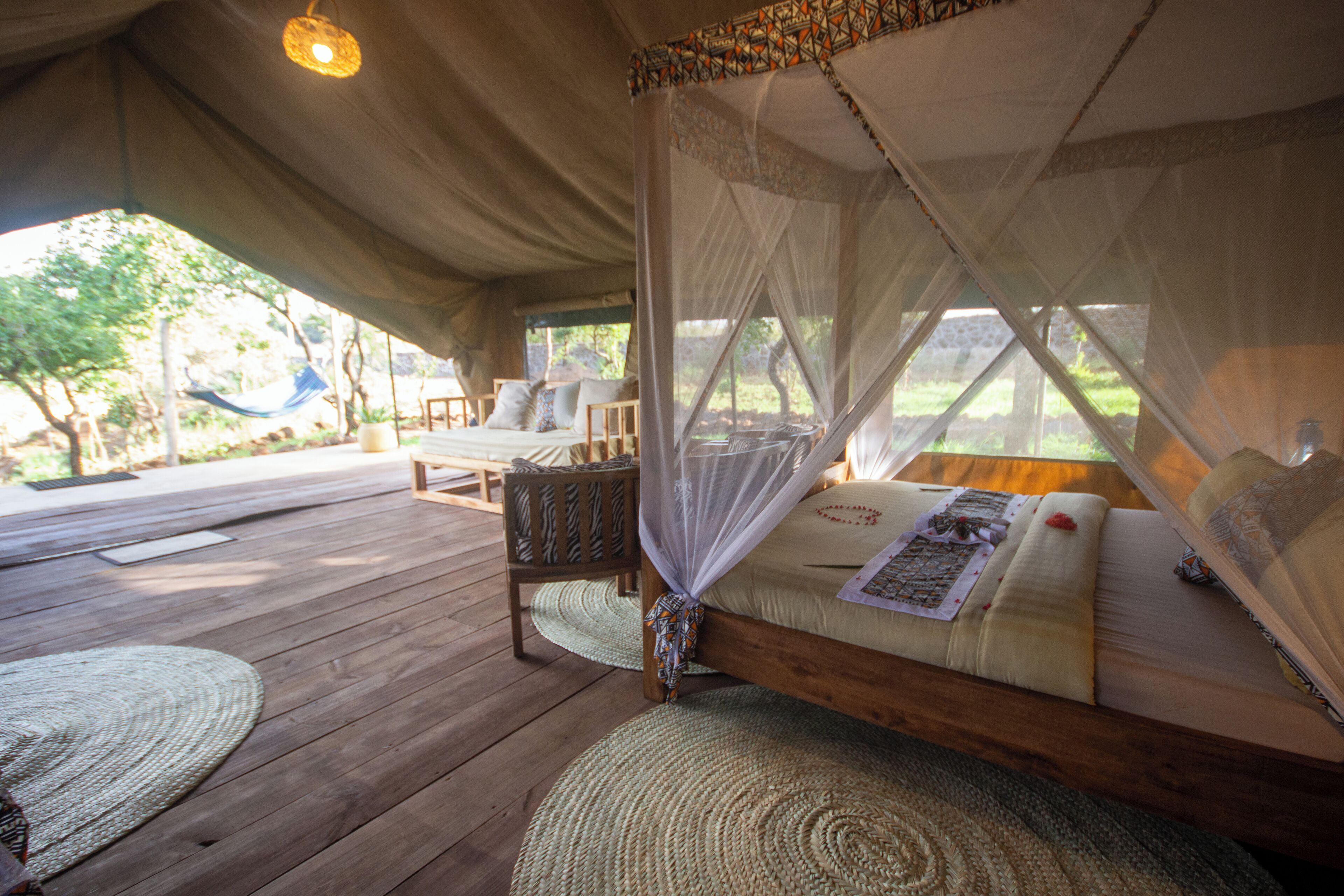 A tented accommodation with a bed, a chair, and a table.