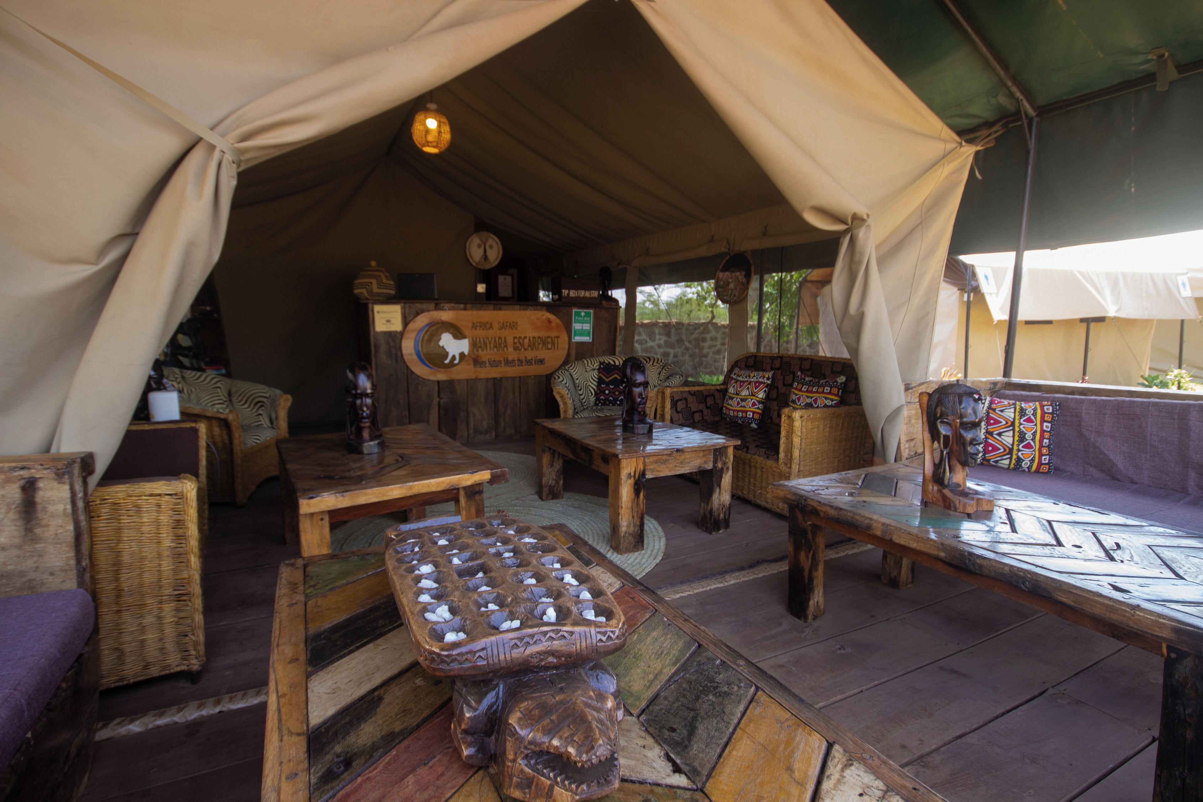 A safari lodge interior with wooden furniture, a central table, and a sign indicating the location.