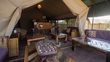 A safari lodge interior with wooden furniture, a central table, and a sign indicating the location.