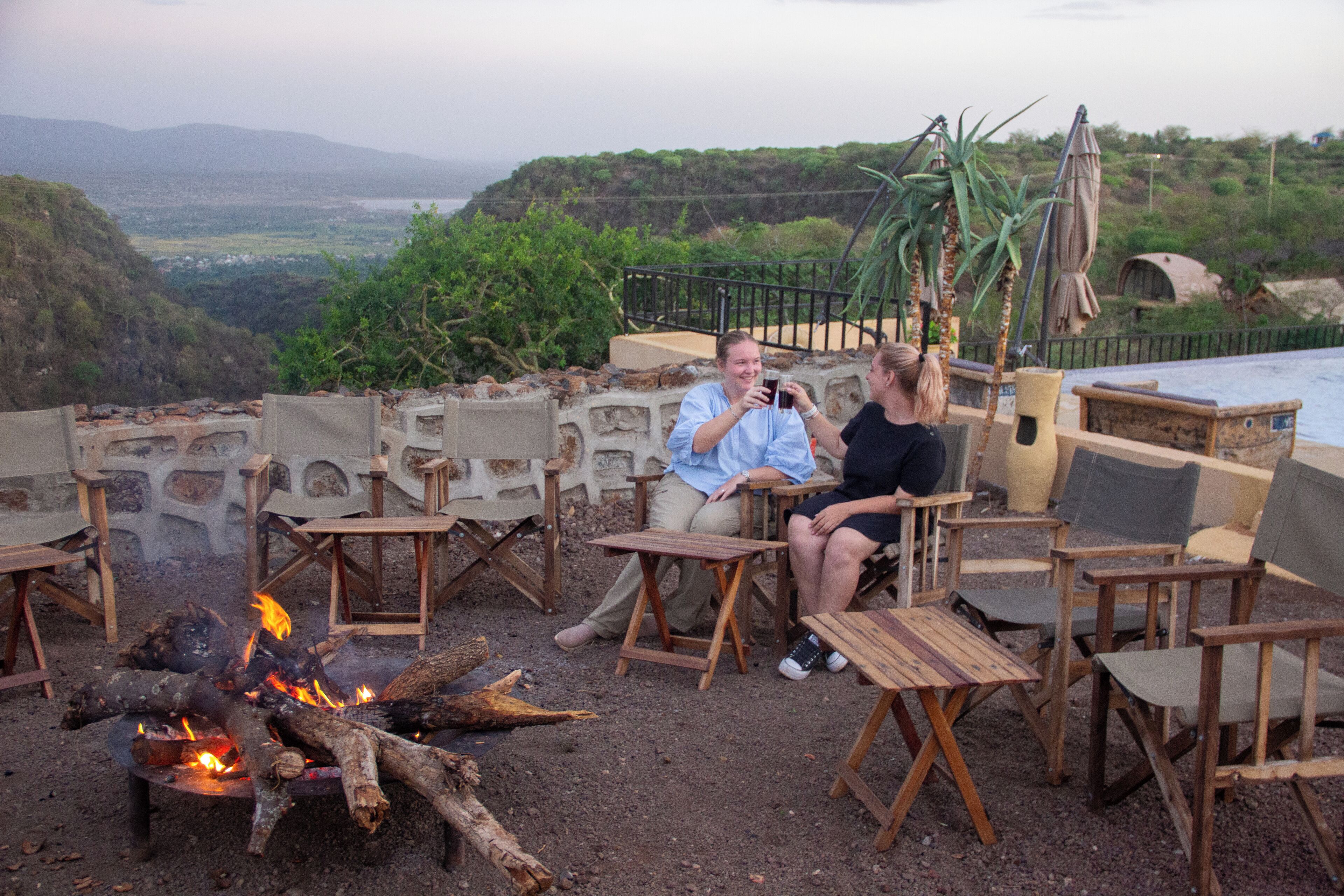 Una terraza con mobiliario de madera, una fogata y vistas del paisaje.