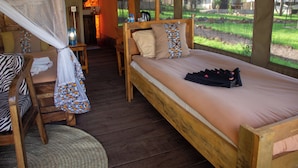 Een houten bed met klamboe, een houten stoel en een klein tafeltje met een lamp.
