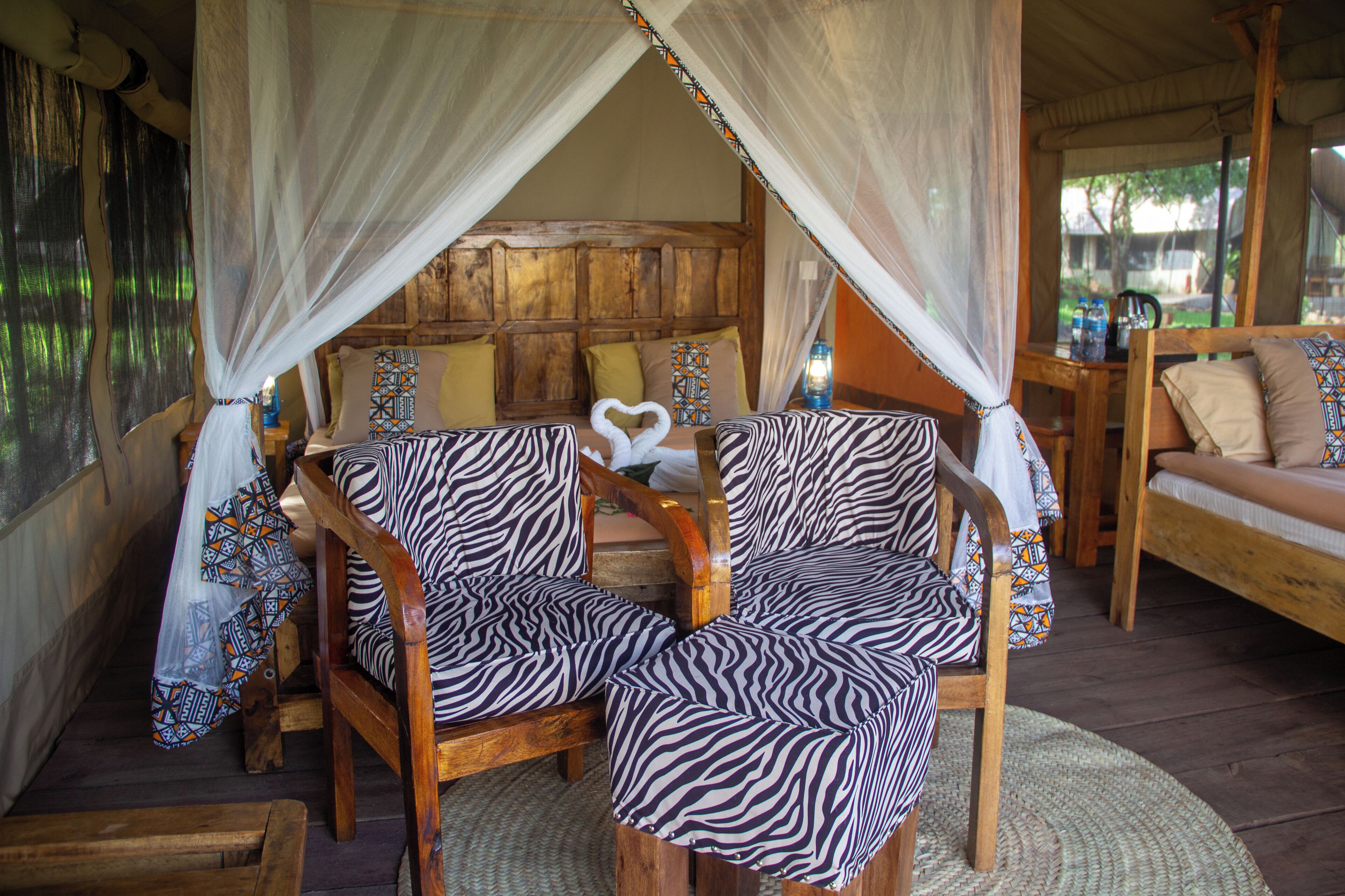 A room with a wooden bed, zebra-patterned chairs, and a canopy bed.