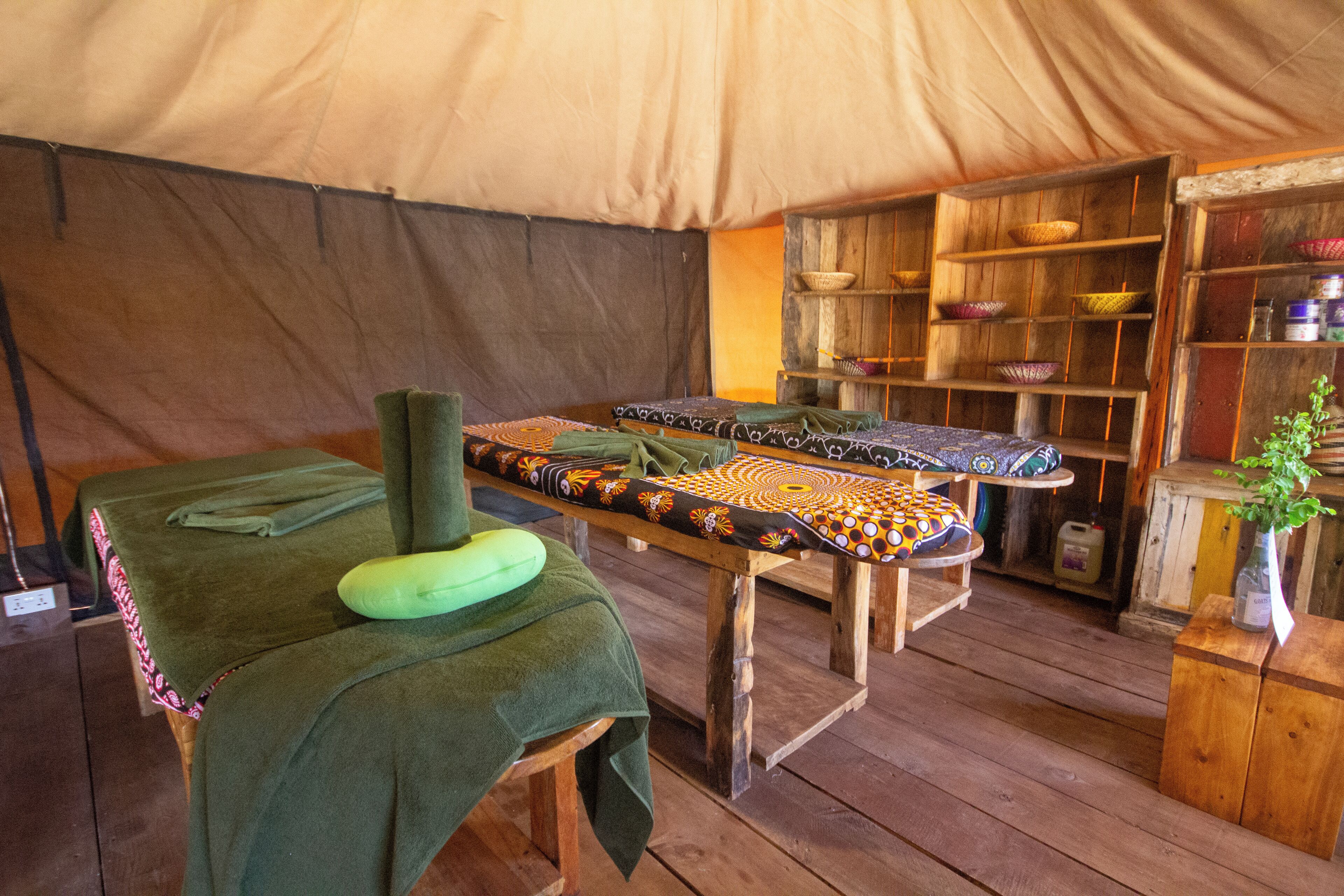 A tented room with a massage table, a green cushion, and shelves with baskets.