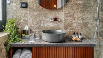 A modern bathroom with a large round sink, a wooden vanity, a mirror, and a shower area.