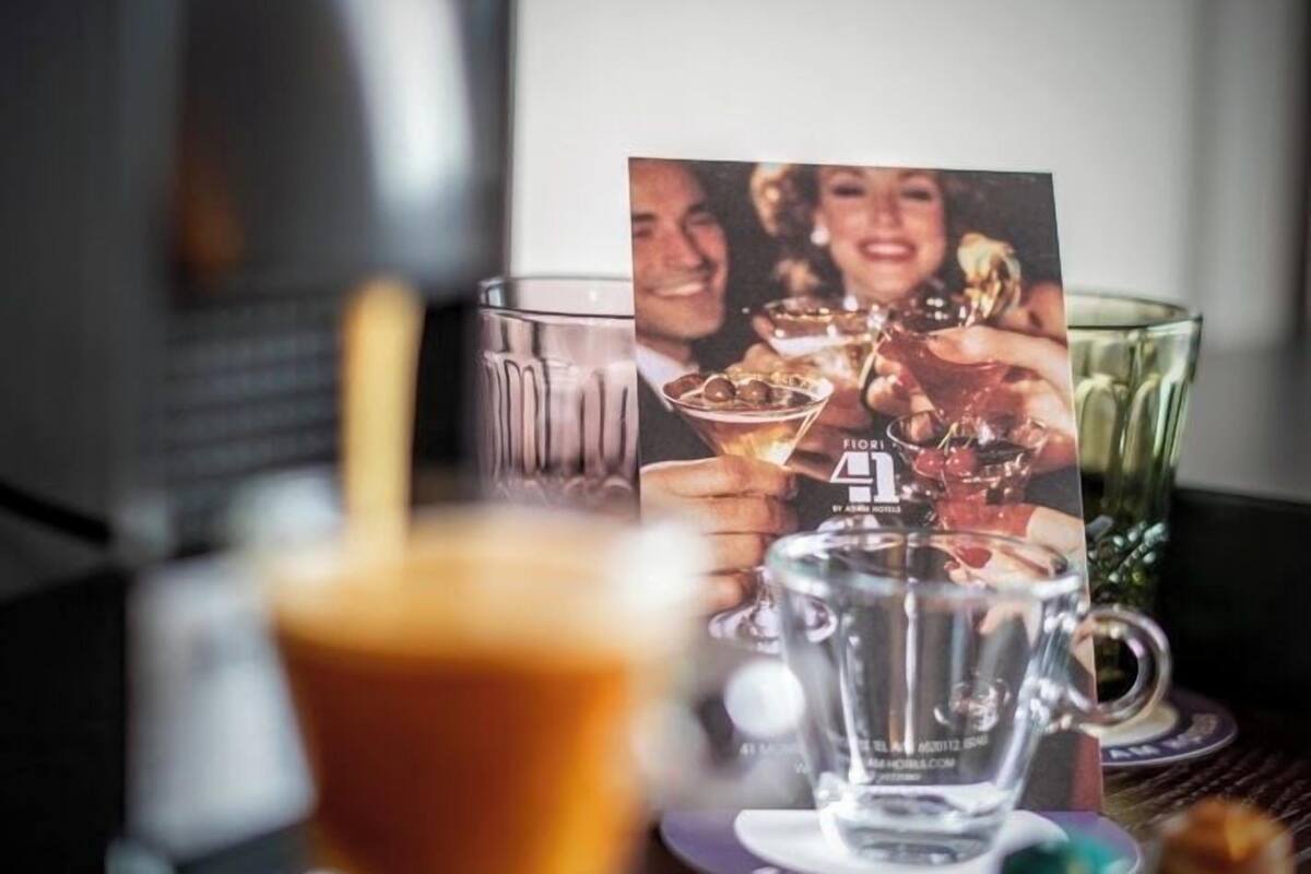 A coffee machine, a glass of coffee, and a card with a photo on a table.