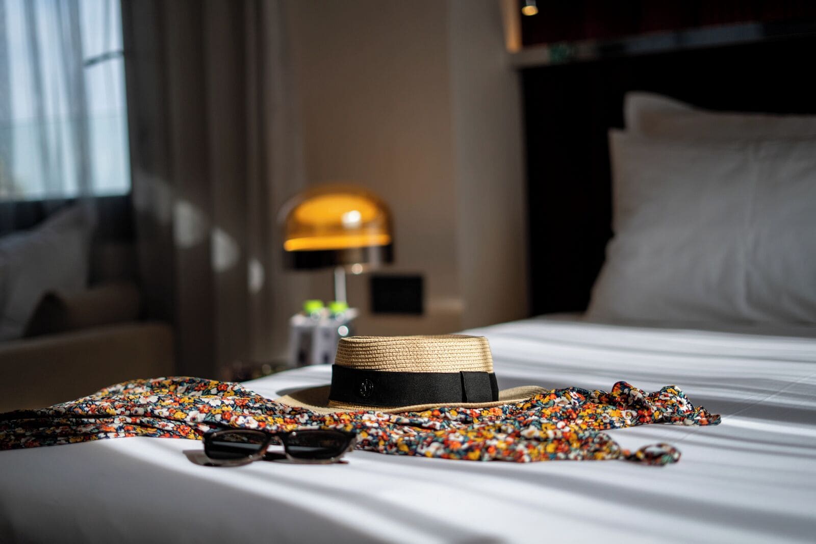 A neatly made bed with a hat, sunglasses, and a colorful scarf on it.
