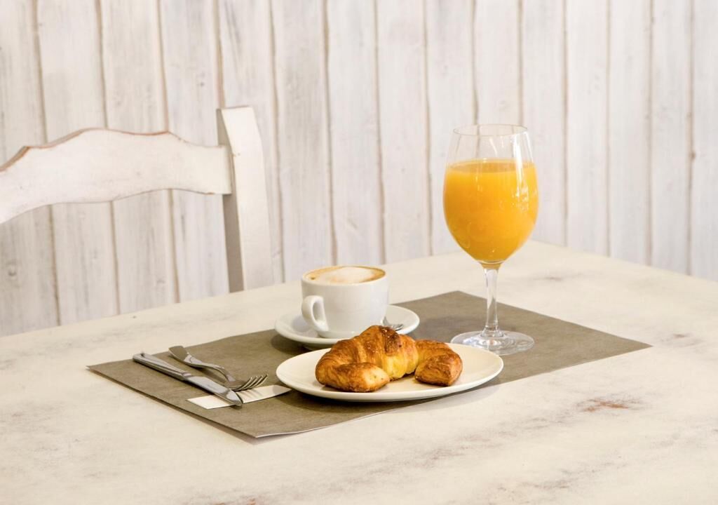 Un desayuno con cruasanes, una taza de café y un vaso de jugo de naranja sobre una mesa de mármol.