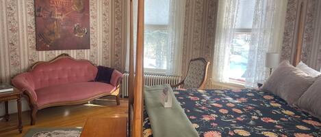 A room with a four-poster bed, a chaise lounge, a radiator, and a floral-patterned rug.