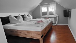 A bedroom with a sloped ceiling, a wooden bed frame, white bedding, and a window with blinds.