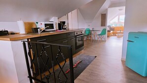 A compact kitchen with modern appliances, a dining area with green chairs, and a teal refrigerator.