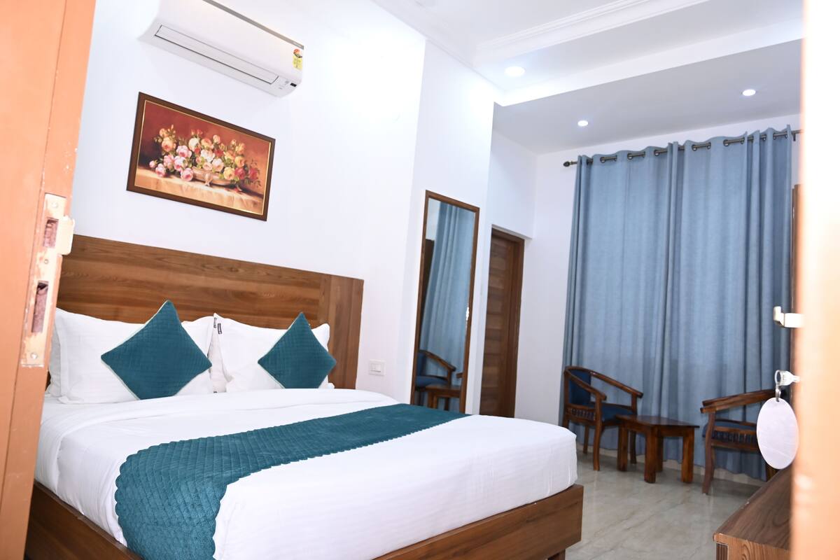 A hotel room with a wooden bed, a painting on the wall, and a view of the outside through a window with curtains.
