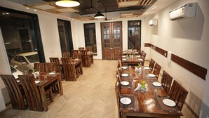 Un comedor con mesas y sillas de madera, suelo con patrón de espiga y luminarias colgantes.