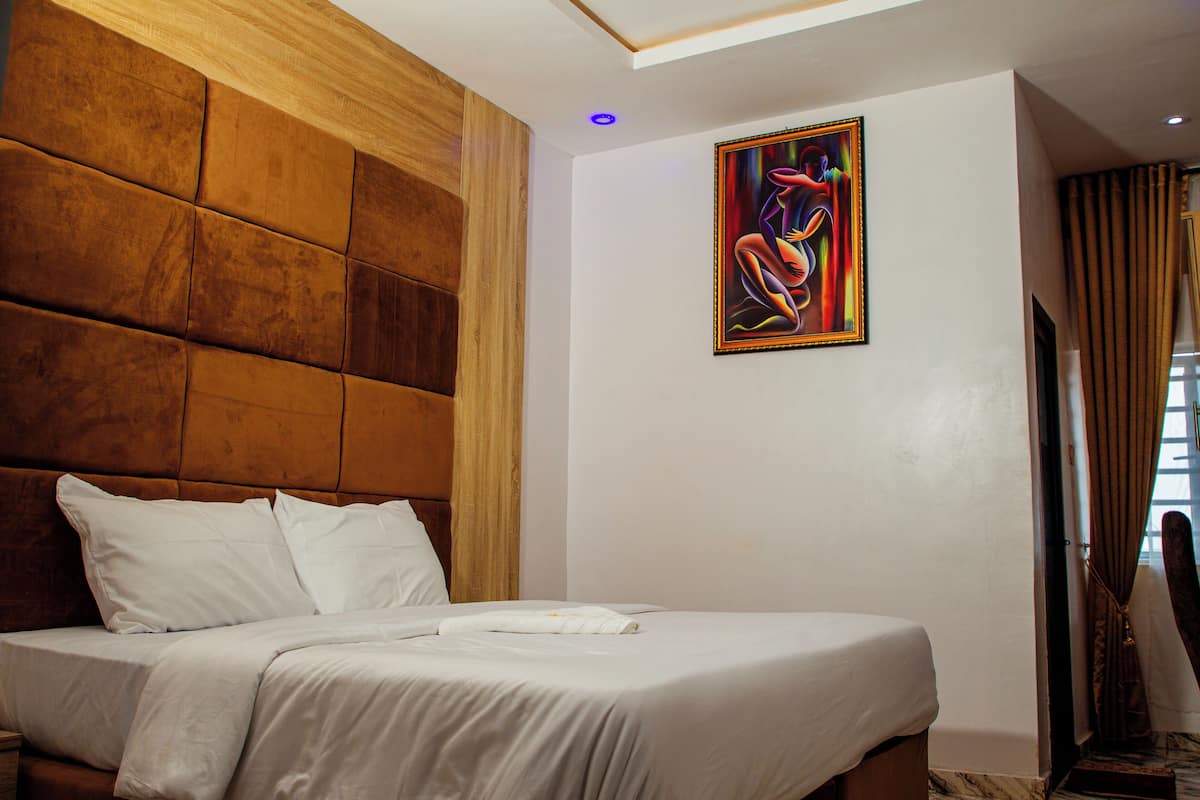 A hotel room with a large bed, a wooden headboard, a painting on the wall, and a window with curtains.