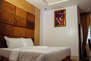 A hotel room with a large bed, a wooden headboard, a painting on the wall, and a window with curtains.