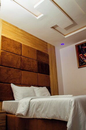 A modern bedroom with a wooden headboard, a bed with white bedding, and a ceiling with recessed lighting.