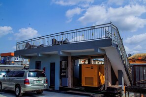 A two-story building with a balcony, a parked car, and a large air conditioning unit outside.