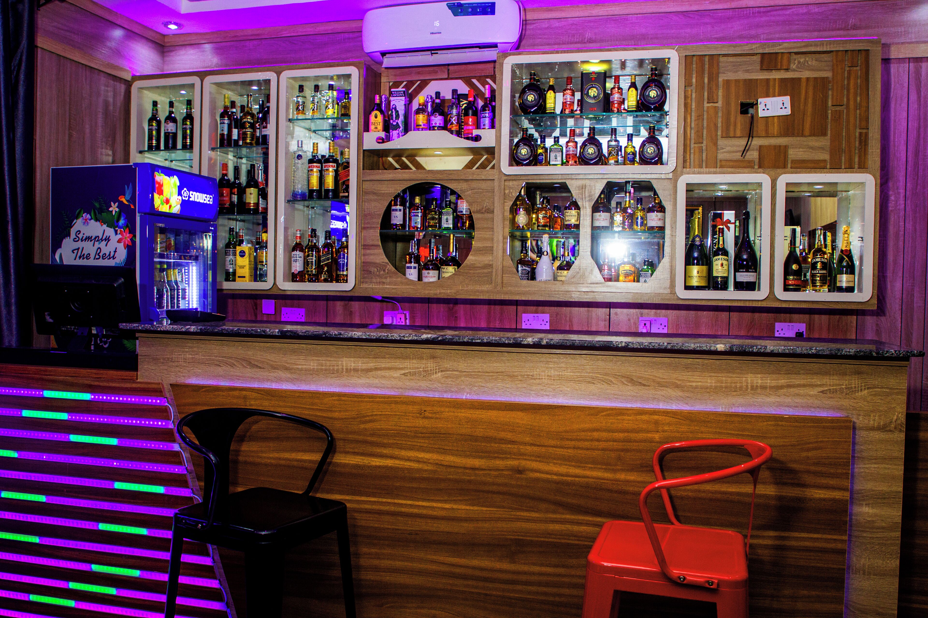 A bar area with multiple shelves of bottles, a refrigerator, and two stools.