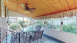 Eine überdachte Terrasse mit Glastisch und Stühlen, einem Deckenventilator und Blick auf einen Hinterhof mit Picknicktisch.