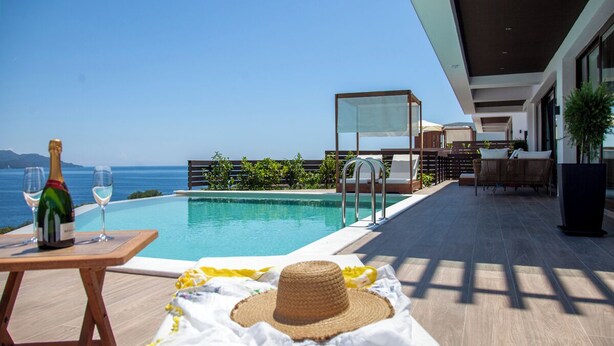 Un área junto a la piscina con vista al mar, una botella de champán y un sombrero de paja sobre una toalla.