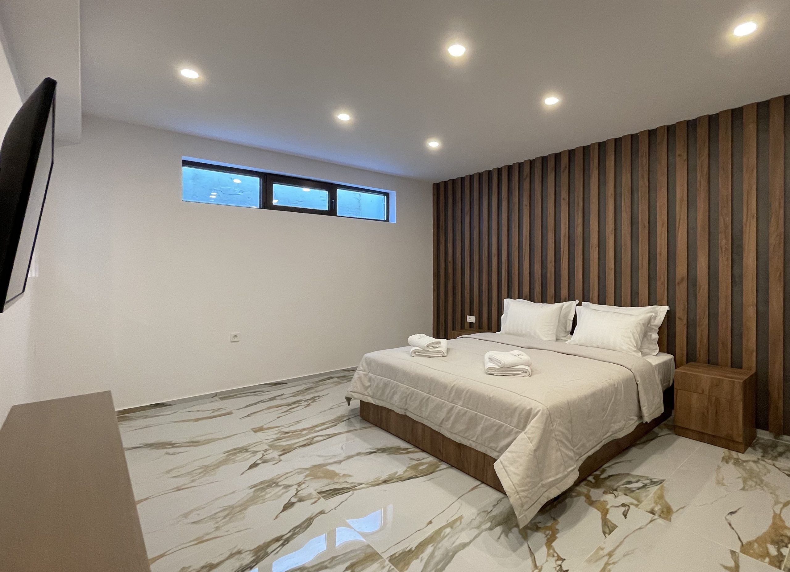 A modern bedroom with a large bed, wooden panel wall, and a window with a view.