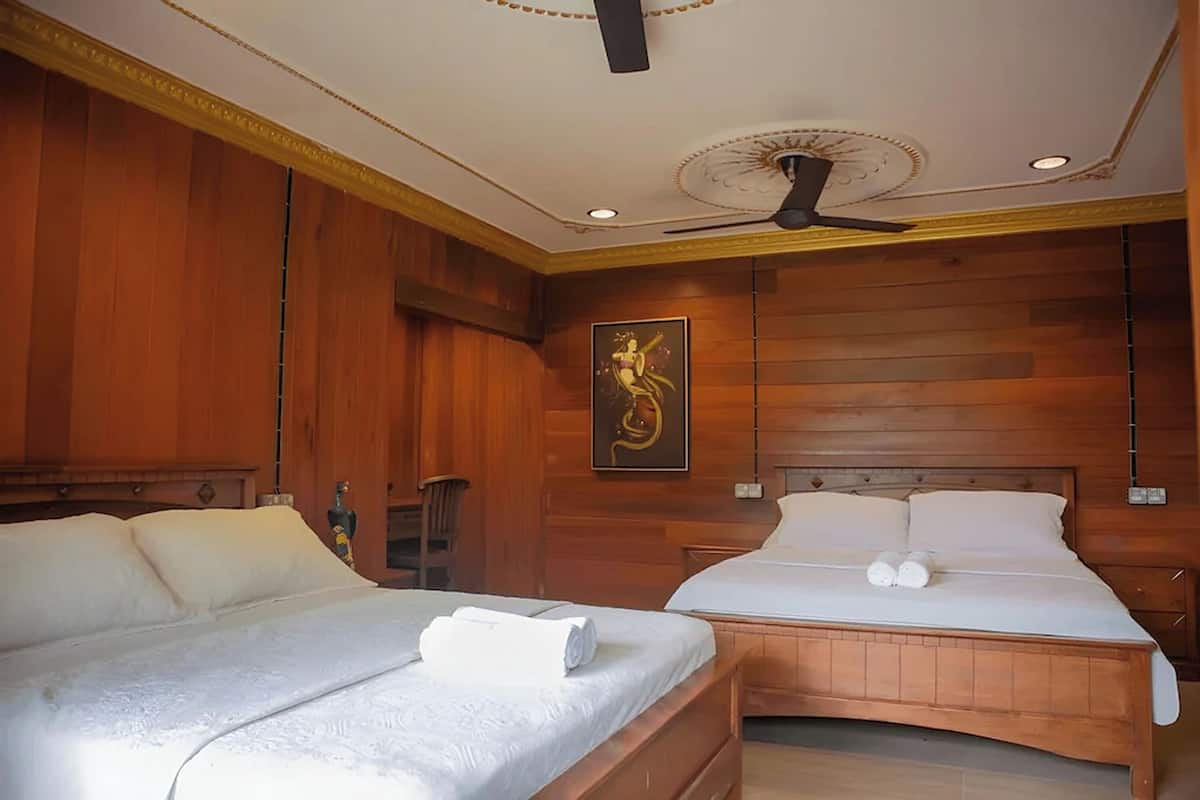 Ein Hotelzimmer mit zwei Betten, Holzvertäfelung, einem Deckenventilator und einem gerahmten Kunstwerk an der Wand.