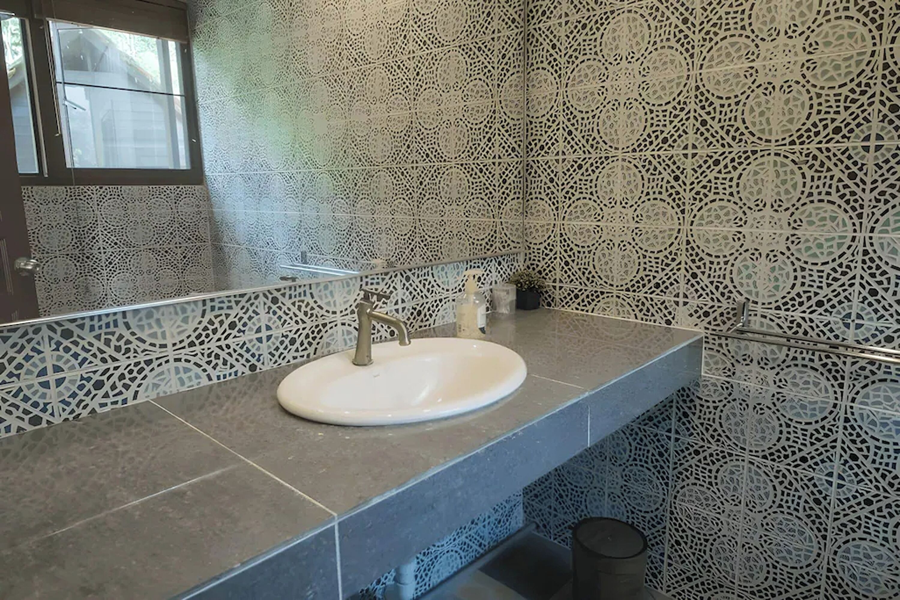 A bathroom with a sink, mirror, and patterned tiles.