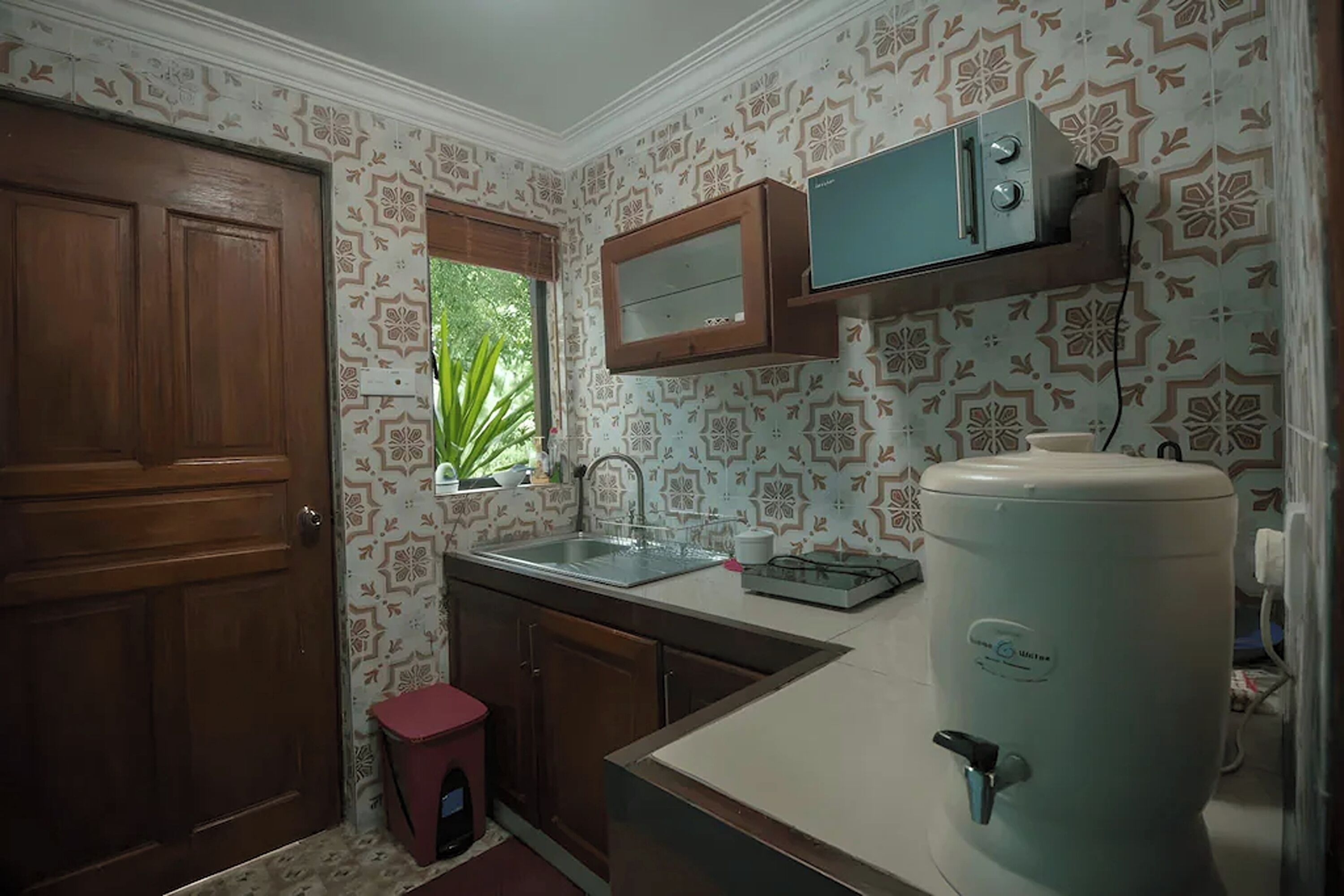 A compact kitchen with a sink, a small window, a cabinet, and a water dispenser.