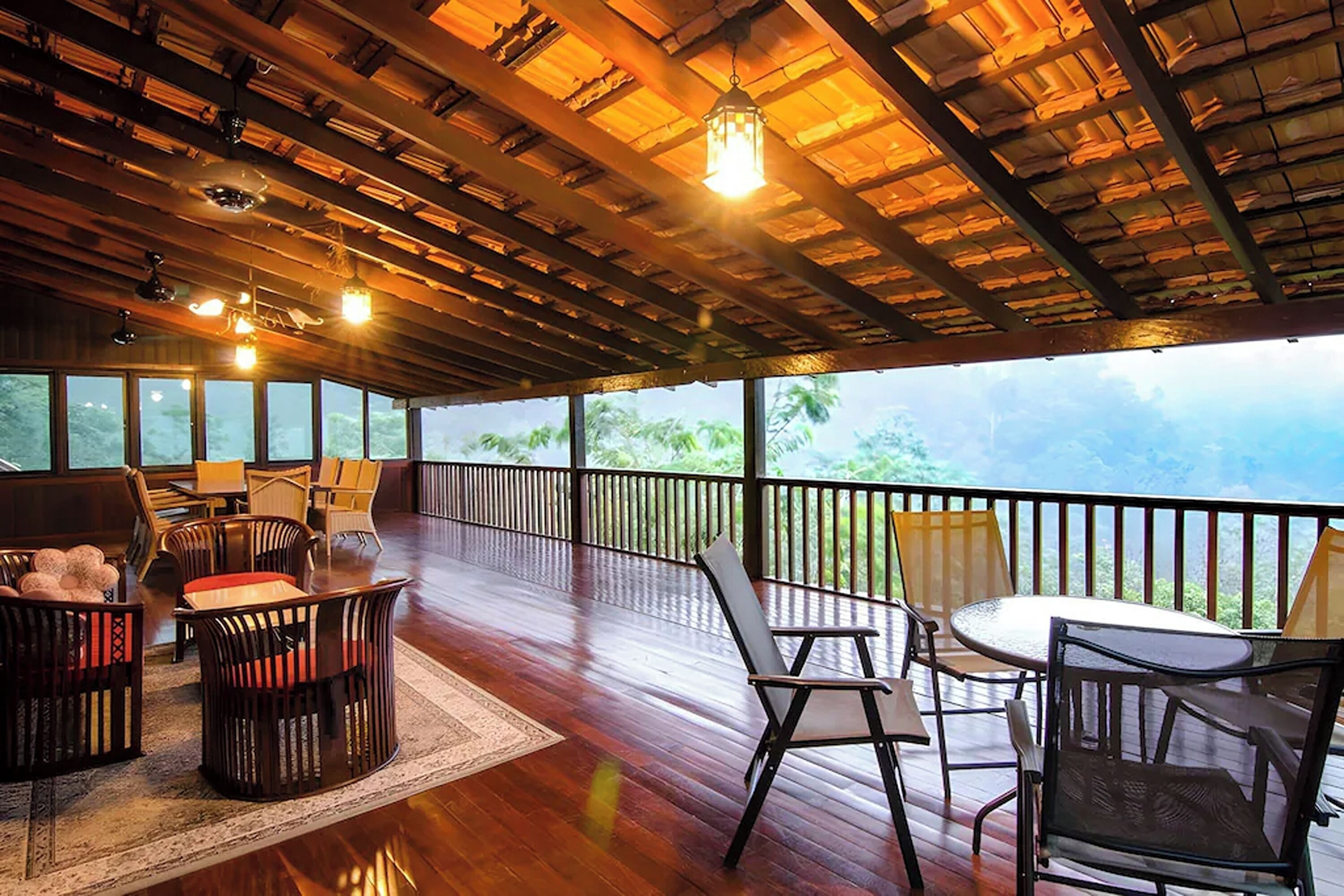 A spacious outdoor area with wooden flooring, multiple seating arrangements, and a view of the surrounding landscape.