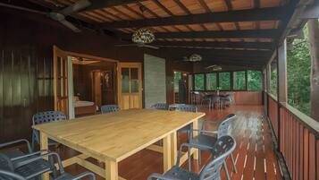Un espacio de comedor al aire libre con techo, una mesa y sillas de madera, un ventilador de techo y vistas al entorno verde.