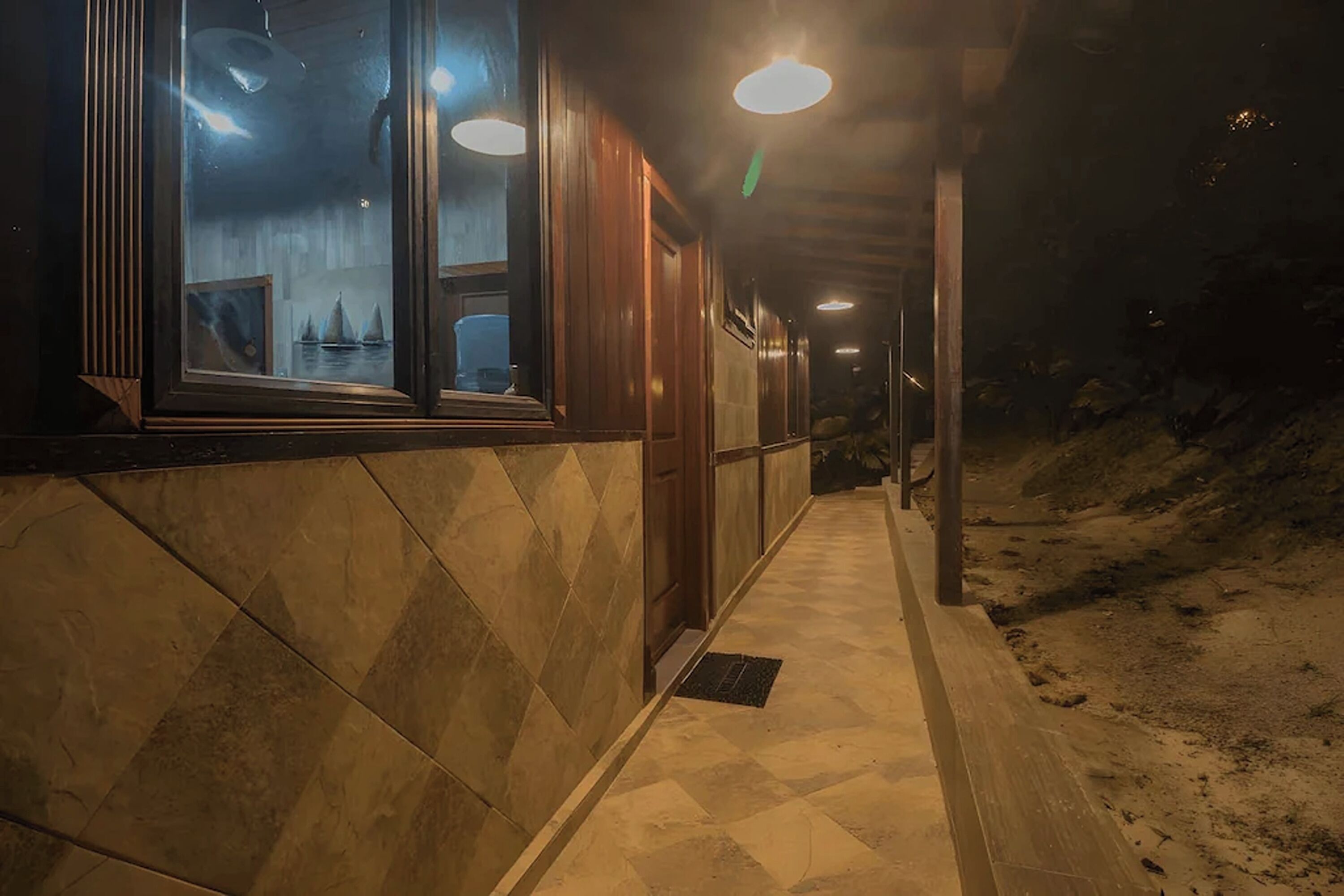 A corridor with tiled flooring, wooden walls, and a window with a view of sailboats.