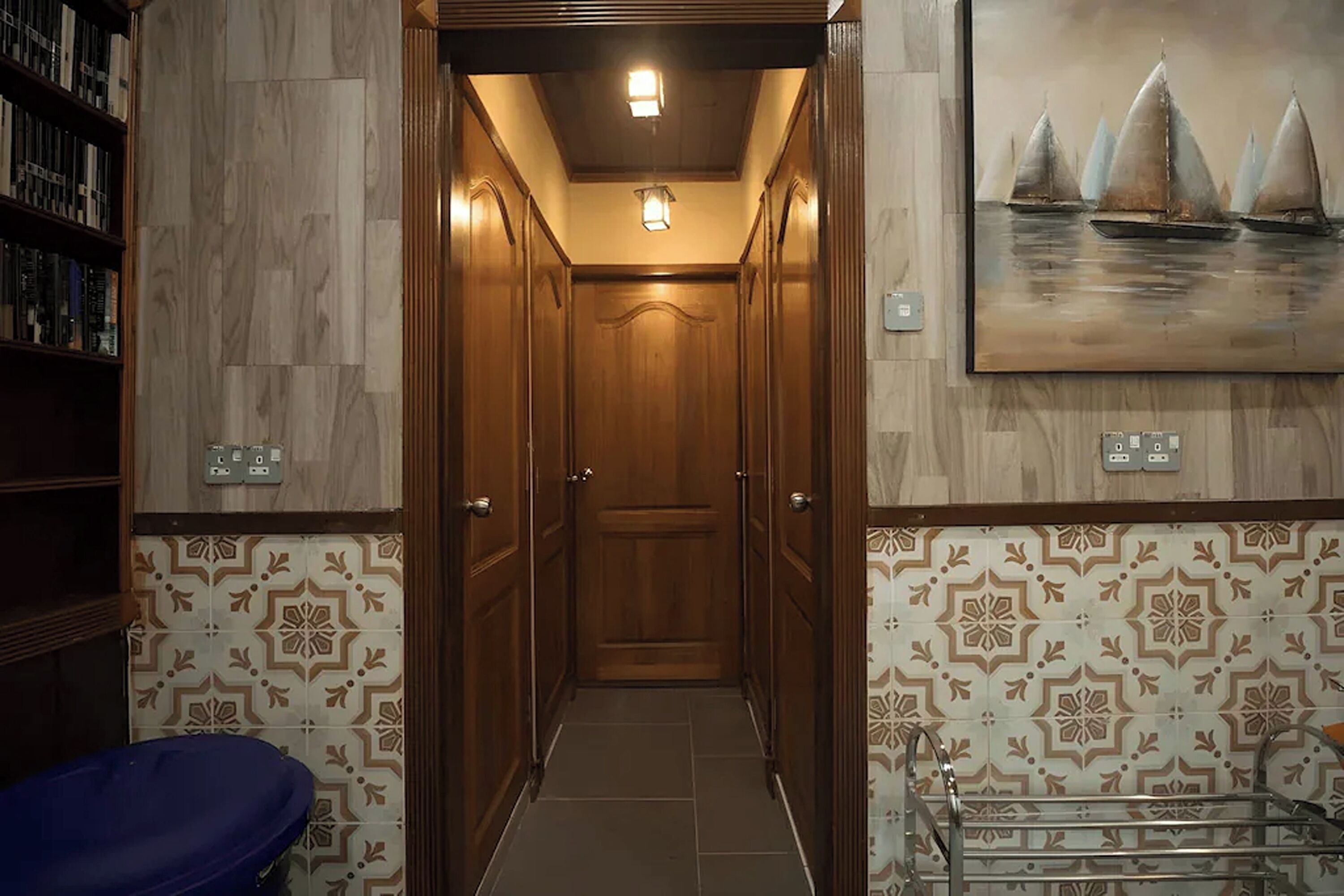 A hallway with patterned walls, a wooden door, and a painting of sailboats.