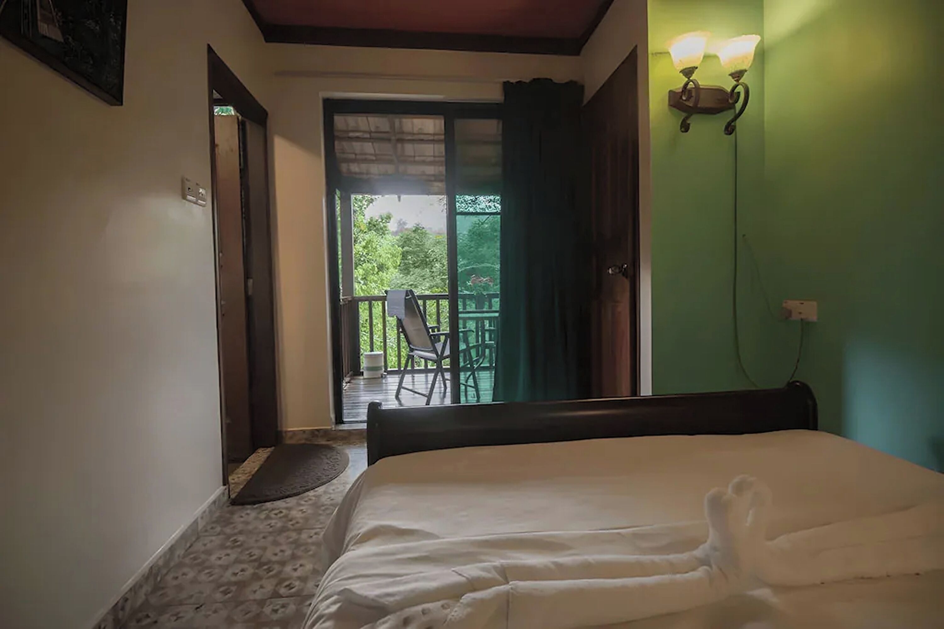 Una habitación con una cama, una puerta que da a un balcón y una lámpara fijada a la pared.