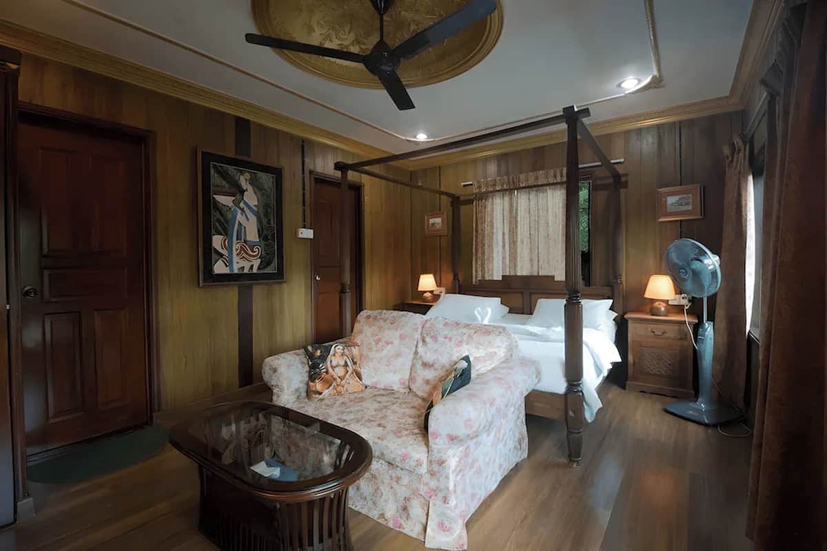 Ein Zimmer mit Bett, Sofa, Deckenventilator, Nachttisch mit Lampe und Holztür.